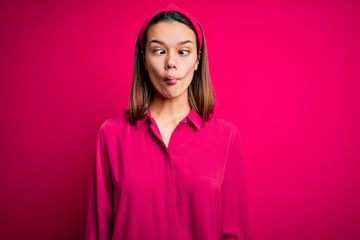 Fototapeta premium Young beautiful brunette girl wearing casual shirt standing over isolated pink background making fish face with lips, crazy and comical gesture. Funny expression.