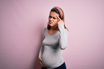 Young beautiful teenager girl pregnant expecting baby over isolated pink background pointing unhappy to pimple on forehead, ugly infection of blackhead. Acne and skin problem
