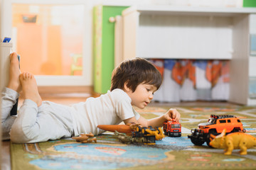 Cute little kid boy playing with lots of toy cars indoor. Happy preschooler having fun at home or nursery. Big collection of different vehicles. Happiness game.