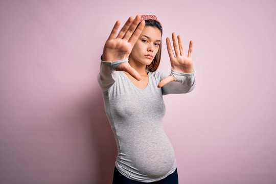 Young beautiful teenager girl pregnant expecting baby over isolated pink background doing frame using hands palms and fingers, camera perspective