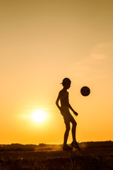 Boy playing with ball in nature in hot evening, silhouette of playing child at sunset in countryside