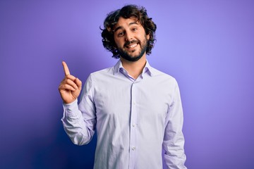 Young handsome business man with beard wearing shirt standing over purple background with a big smile on face, pointing with hand finger to the side looking at the camera.