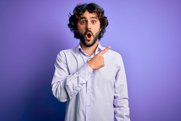 Young handsome business man with beard wearing shirt standing over purple background Surprised...