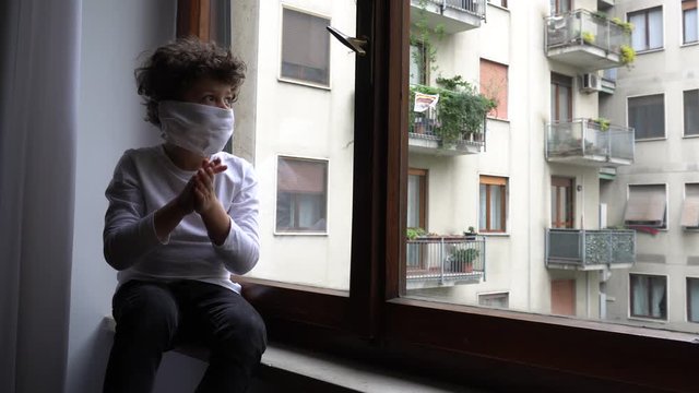Europe, Italy , Milan -  children boy  five years with mask at home during quarantine at home due n-cov19 Coronavirus outbreak - life style in apartment - look and say hello from the window rainy day