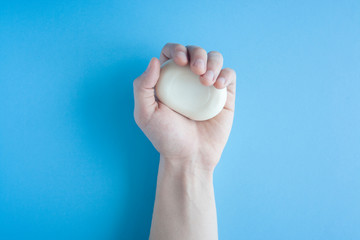 A piece of soap in a male hand a top view on a blue background. The human hand holds soap. Wash your hands. Soap against bacteria and viruses. Compliance with hygiene and sterility to combat 