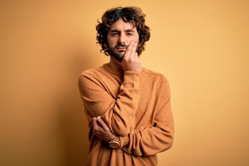 Fototapeta na wymiar Young handsome man with beard wearing casual sweater standing over yellow background thinking looking tired and bored with depression problems with crossed arms.