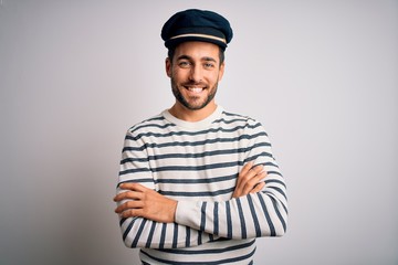 Young handsome sailor man with beard wearing navy striped uniform and captain hat happy face smiling with crossed arms looking at the camera. Positive person. - obrazy, fototapety, plakaty