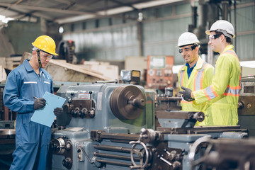 Three technician inspecting complex metal component at machine in factory