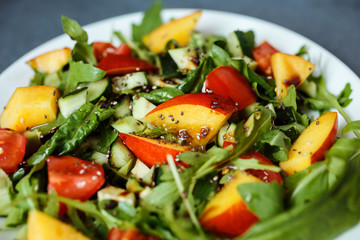 Close up food photo of the healthy salad made of arugula, cherry tomatoes, spinach, avocado, nectarine, chia seeds and sprinkled with olive oil and balsamic vinegar.