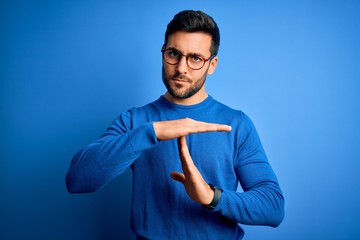 Young handsome man with beard wearing casual sweater and glasses over blue background Doing time...