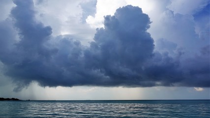 Waiting for a thunderstorm. Maldives. A large dark blue cloud hung over the ocean. The ocean is calm. An island is visible in the distance. Everything is quiet.
