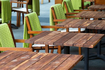 View of a row of empty wooden tables in a street cafe next to which are chairs with green rugs. Concept city, cafe, catering, crisis.