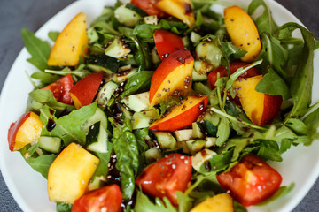 Close up photo of the colorful summer salad. Healthy salad contains ruccola, cherry tomatoes, spinach, avocado, nectarine, chia seeds. It is sprinkled with olive oil and balsamic vinegar.