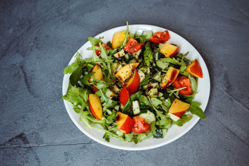 Colorful summer salad made of arugula, spinach, avocado, nectarine, chia seeds. Salad on the white plate on the gray background.