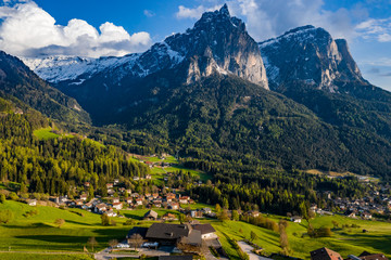 Fototapeta na wymiar Aerial view of improbable green meadows of Italian Alps, green slopes of the mountains, Bolzano, huge clouds over a valley, roof tops of houses, Dolomites on background, sunshines through clouds