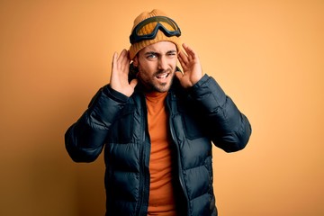 Young handsome skier man with beard wearing snow sportswear and ski goggles Trying to hear both hands on ear gesture, curious for gossip. Hearing problem, deaf