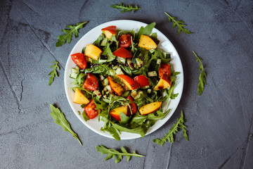 Flat lay photo of healthy colorful salad on the white plate on the gray background. Arugula,spinach, avocado, nectarine, chia seeds and cherry tomatoes on the plate.