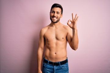 Fototapeta premium Young handsome strong man with beard shirtless standing over isolated pink background smiling positive doing ok sign with hand and fingers. Successful expression.