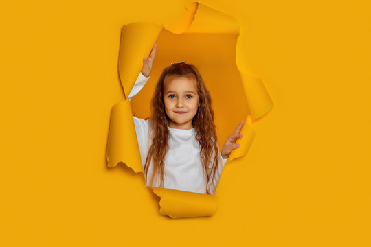 Portrait of cute happy smiling caucasian little cild girl poses in yellow paper hole.