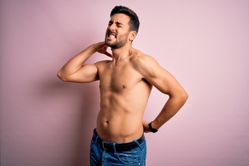 Fototapeta premium Young handsome strong man with beard shirtless standing over isolated pink background Suffering of neck ache injury, touching neck with hand, muscular pain