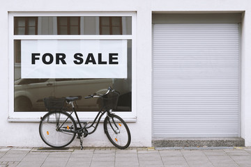 for sale sign in store window with bicycle parked outside - shop vacancy due to business closure -...