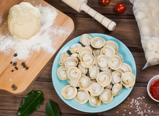 Semi-finished dumplings on a plate on wooden background