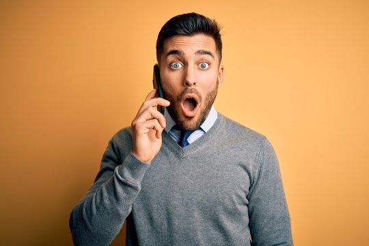 Young handsome man having conversation talking on the smartphone over yellow background scared in shock with a surprise face, afraid and excited with fear expression