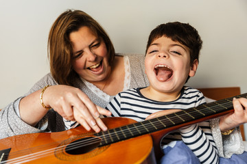niño juega y aprende con  una mujer a tocar la guitarra en la cama. son madre e hijo, él tiene...