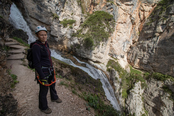 A woman standing on a trail in the Dolomites with a waterfall in the background