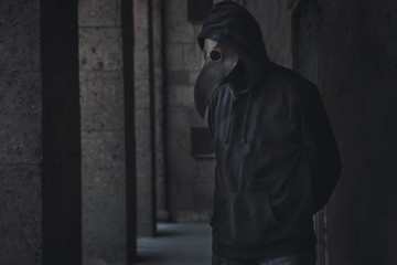 Dark horror figure in black hood in plague doctor mask on the grunge background. Stylized epidemic...