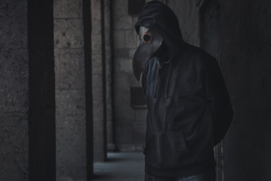 Dark horror figure in black hood in plague doctor mask on the grunge background. Stylized epidemic costume
