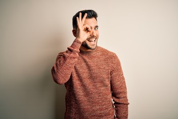 Young handsome man wearing casual sweater standing over isolated white background doing ok gesture with hand smiling, eye looking through fingers with happy face.
