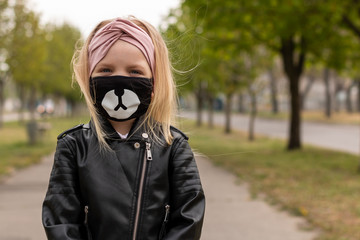Baby girl in a hygiene mask is walking on a street