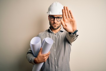 Young architect man wearing contractor helmet holding project paper plan over isolated background...