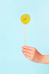Yellow lollipop in woman hand on blue background. Girls hold hard candy caramel on stick, sweets holidays concept, copy space for text, minimal, summer creative idea - sun and blue sky