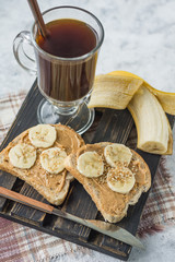 Sandwiches with peanut butter and banana and coffee for breakfast on a wooden stand