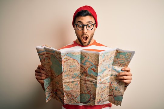 Young handsome tourist man on vacation wearing glasses holding city map scared in shock with a surprise face, afraid and excited with fear expression
