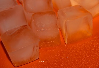 Pieces of ice on a bright background with water drops. Orange fresh background with ice cubes.