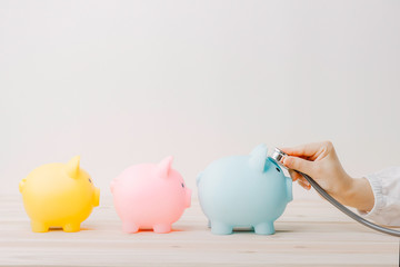 Doctor using stethoscope to check 3 piggy bank in queue. Concept check saving money and financial sustainability