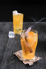 Two glasses of hot orange punch with ice, cinnamon sticks on a wooden background. Free space for text
