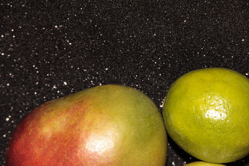 Fototapeta na wymiar Fruit on a black shiny background. Green fruit on a black background. Mango red-green and lime with Apple