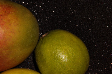 Fototapeta na wymiar Fruit on a black shiny background. Green fruit on a black background. Mango red-green and lime.