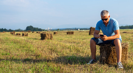 Adult man with a phone sits on a haystack.