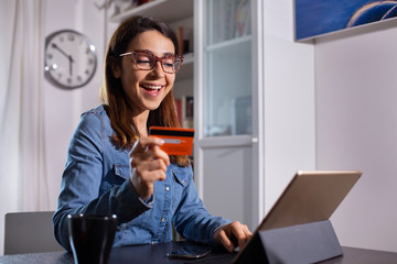 ragazza con occhiali fa un ordine con la carta di credito seduta di fronte al suo iPad a casa sua - obrazy, fototapety, plakaty