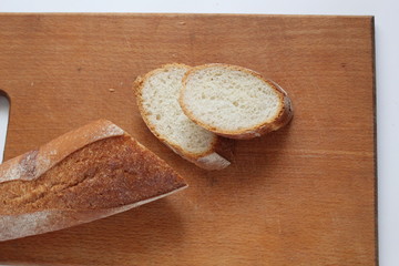 on a wooden Board there is a baguette and two cut pieces of white bread baguette