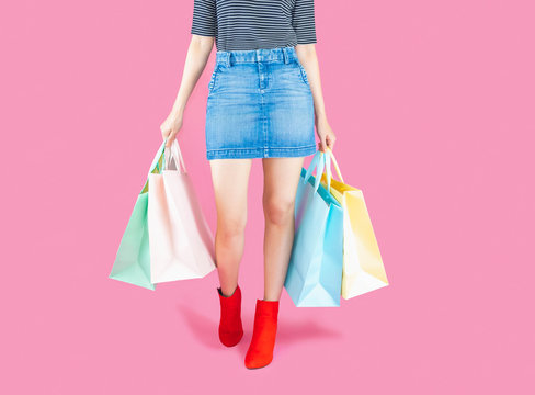 The woman low body part wore Denim skirt and red boots. Carrying a shopping bag in many pastel colors on pink background selective focus with copy space