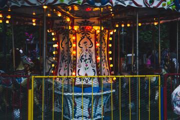 Obraz na płótnie Canvas Children's carousel with burning lights and fenced with a metal fence