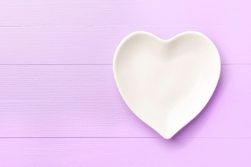 Empty white heart-shaped plate on a pink bright wooden plank background. Abstract template for holiday valentines day. Close-up. Love concept