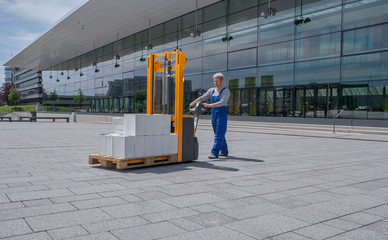 man in overalls operates an electric stacker loaded with boxes