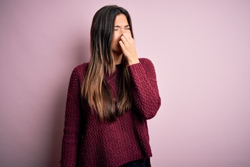 Young beautiful girl wearing casual sweater over isolated pink background smelling something stinky...